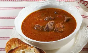 Aksamitna, aromatyczna najlepsza zupa gulaszowa z kawałkami mięsa w głębokim, czerwonym sosie, podana z chrupiącym pieczywem.