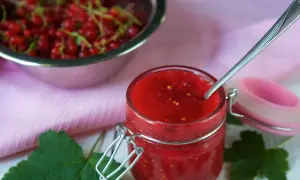 Słoiczek z domowym dżemem z czerwonej porzeczki bez pestek, obok miska pełna świeżych owoców.