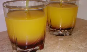 Dwa szklanki z żółtym drinkiem i ciemnym dnem, na marmurowym blacie.