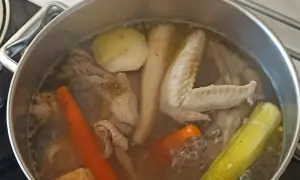 Gotowanie rosołu bez przykrycia. W garnku bulgoczą kawałki kurczaka, marchewka, por i inne warzywa.