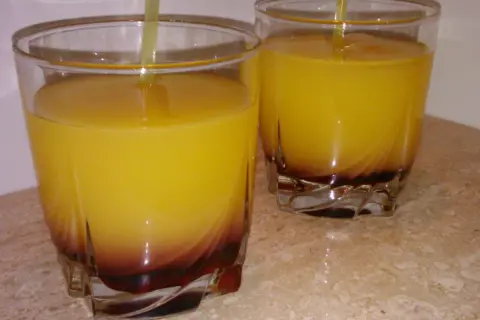 Dwa szklanki z żółtym drinkiem i ciemnym dnem, na marmurowym blacie.