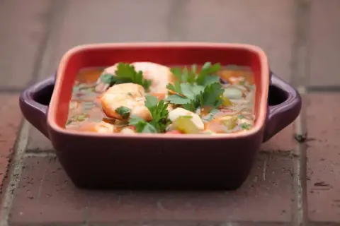 Gęste, aromatyczne gumbo z krewetkami i ziołami, podane w małej, kwadratowej miseczce z uchwytami.