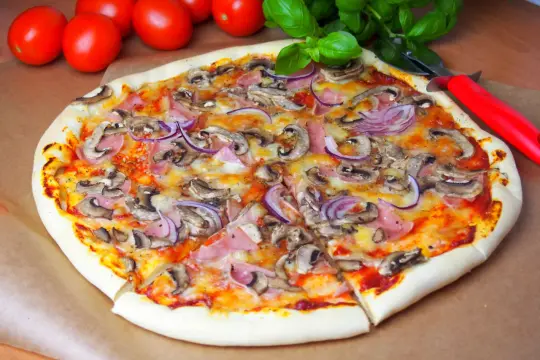 Pyszna pizza capricciosa z pieczarkami, szynką i czerwoną cebulą, gotowa do podania.