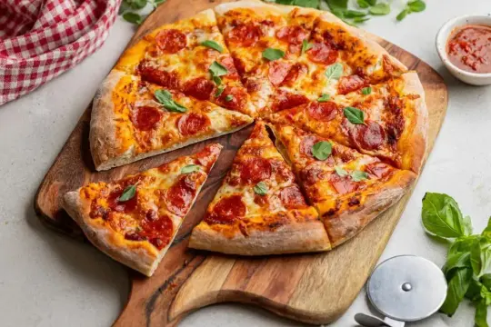 Apetyczna pizza pepperoni z ciągnącym serem i świeżą bazylią, pokrojona na kawałki, czeka na desce.