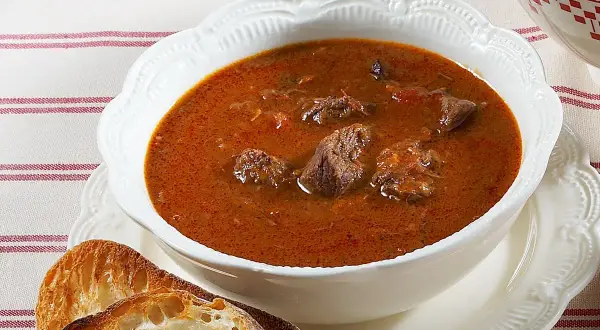 Aksamitna, aromatyczna najlepsza zupa gulaszowa z kawałkami mięsa w głębokim, czerwonym sosie, podana z chrupiącym pieczywem.