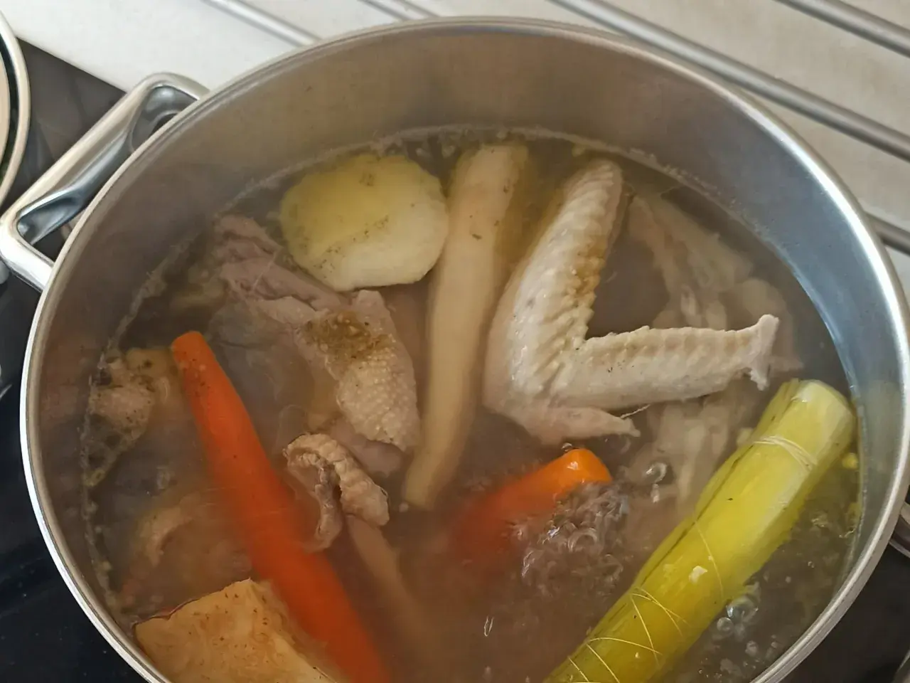 Gotowanie rosołu bez przykrycia. W garnku bulgoczą kawałki kurczaka, marchewka, por i inne warzywa.