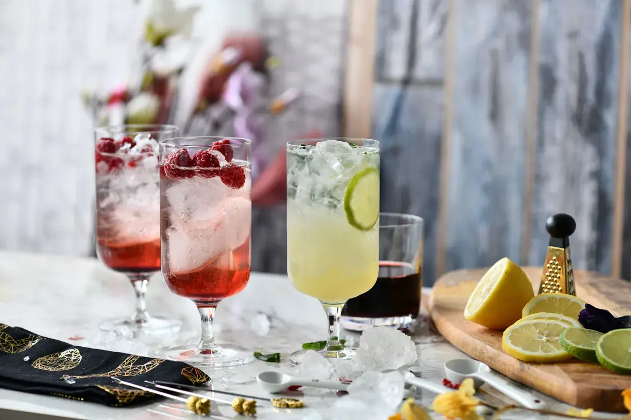 Trzy orzeźwiające drinki z malinami i limonką, ozdobione owocami i lodem.