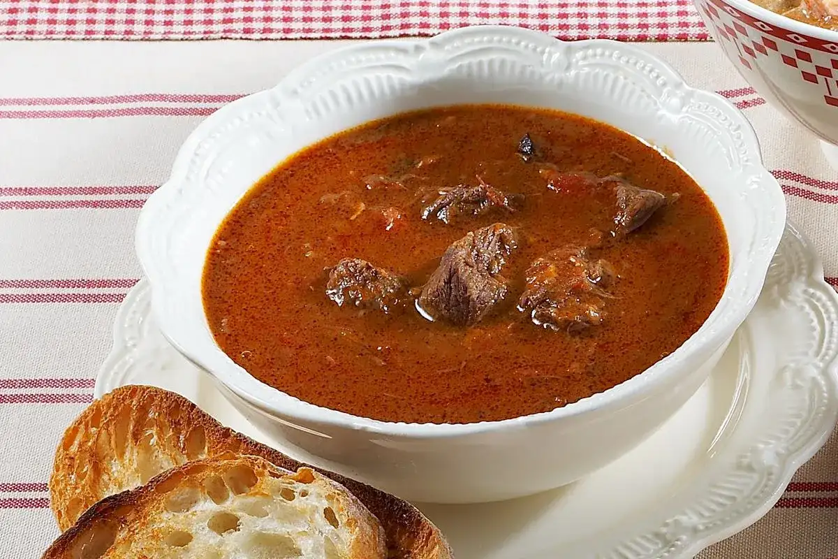Aksamitna, aromatyczna najlepsza zupa gulaszowa z kawałkami mięsa w głębokim, czerwonym sosie, podana z chrupiącym pieczywem.