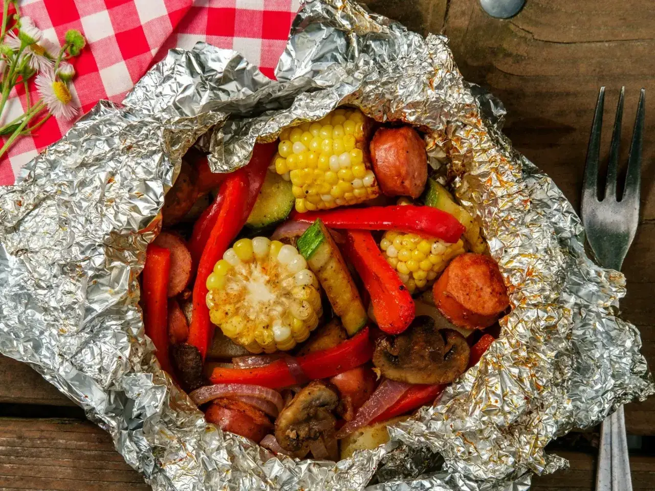 Pyszna kiełbasa podwawelska z warzywami z grilla, zapakowana w folię aluminiową. Kolby kukurydzy, papryka i pieczarki tworzą apetyczną kompozycję.