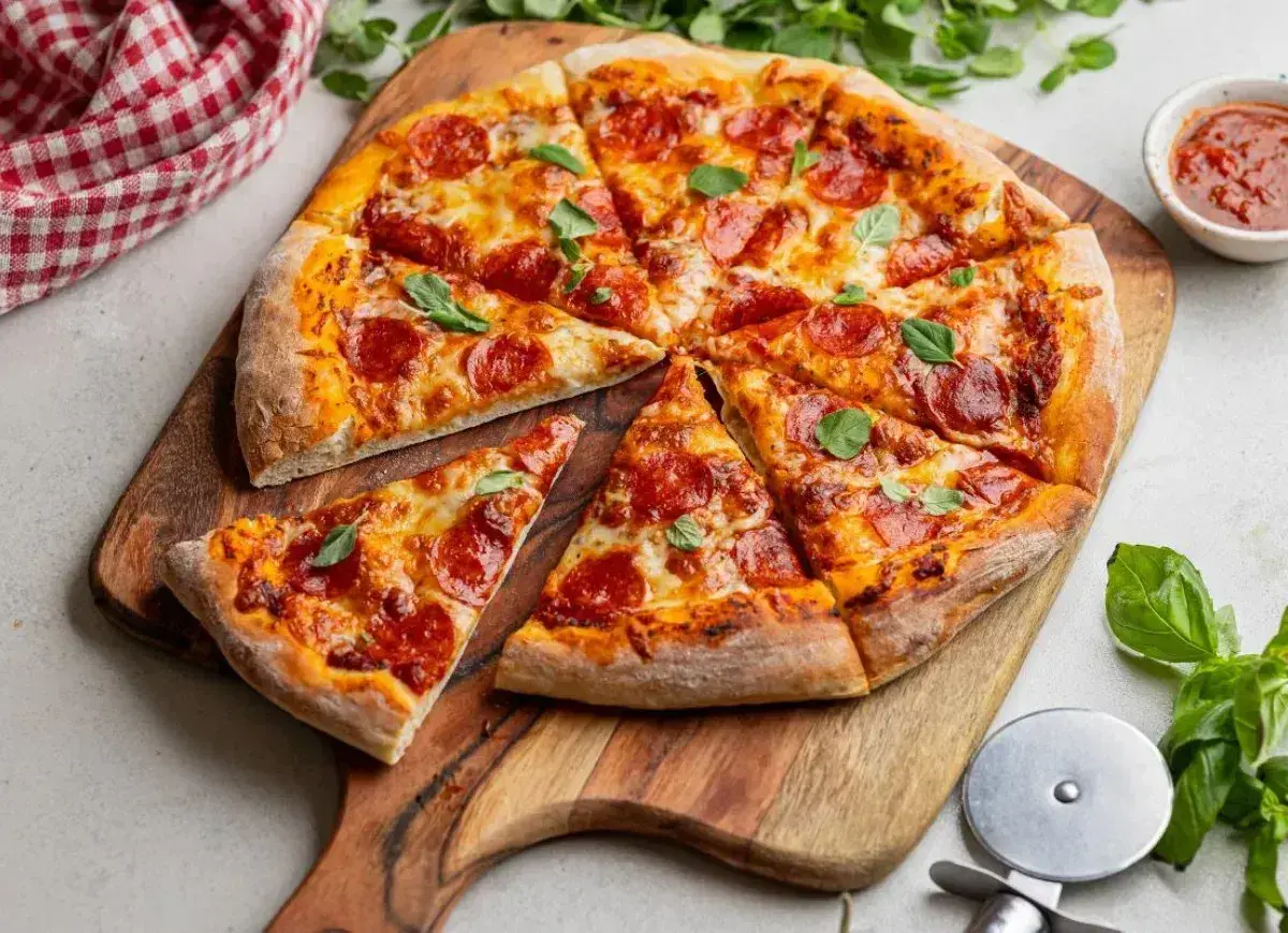 Apetyczna pizza pepperoni z ciągnącym serem i świeżą bazylią, pokrojona na kawałki, czeka na desce.