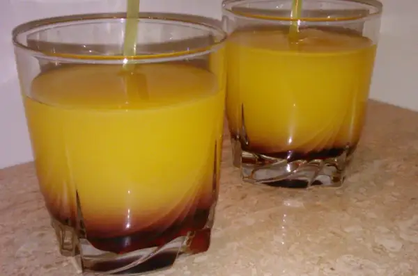Dwa szklanki z żółtym drinkiem i ciemnym dnem, na marmurowym blacie.