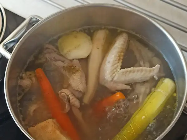 Gotowanie rosołu bez przykrycia. W garnku bulgoczą kawałki kurczaka, marchewka, por i inne warzywa.