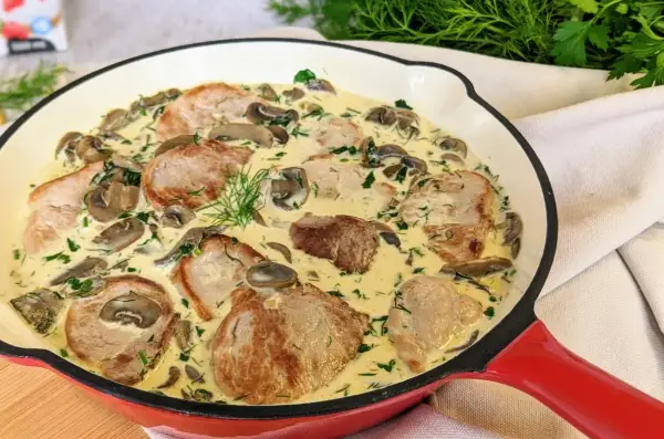 Miękkie polędwiczki wieprzowe w sosie grzybowym, udekorowane koperkiem. Pyszne danie w czerwonej patelni.